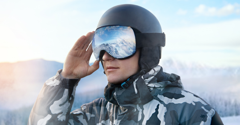 Asmuo dėvi slidinėjimo akinius ir šalmą su kalnų atspindžiu