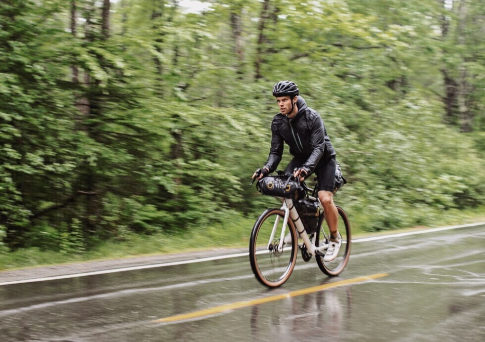 Dviratininkas važiuoja per lietų miško keliu